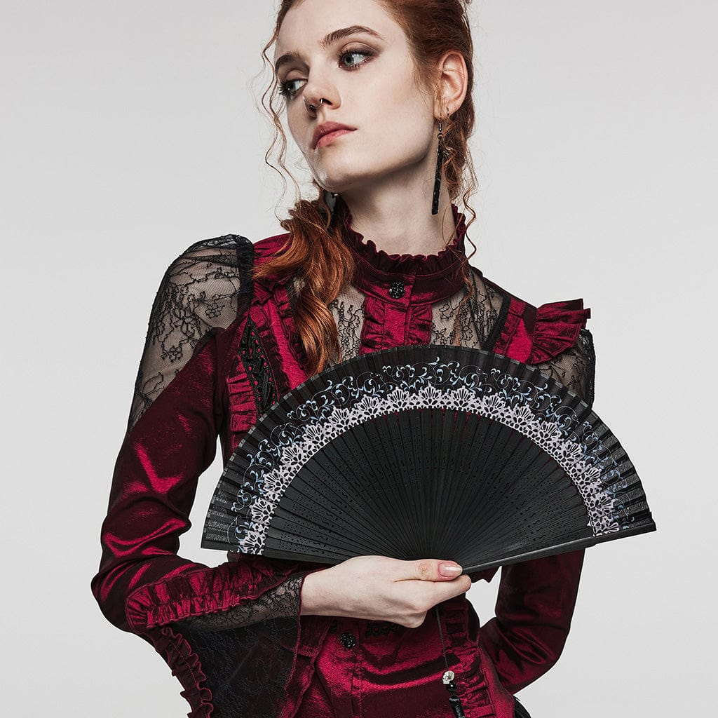 The model gracefully holds the Enchanted folding hand fan, showcasing its black wooden monture, lace detailing, and tassel with skull bead. The fan's ornate cut-outs and fabric leaves complete the gothic aesthetic.